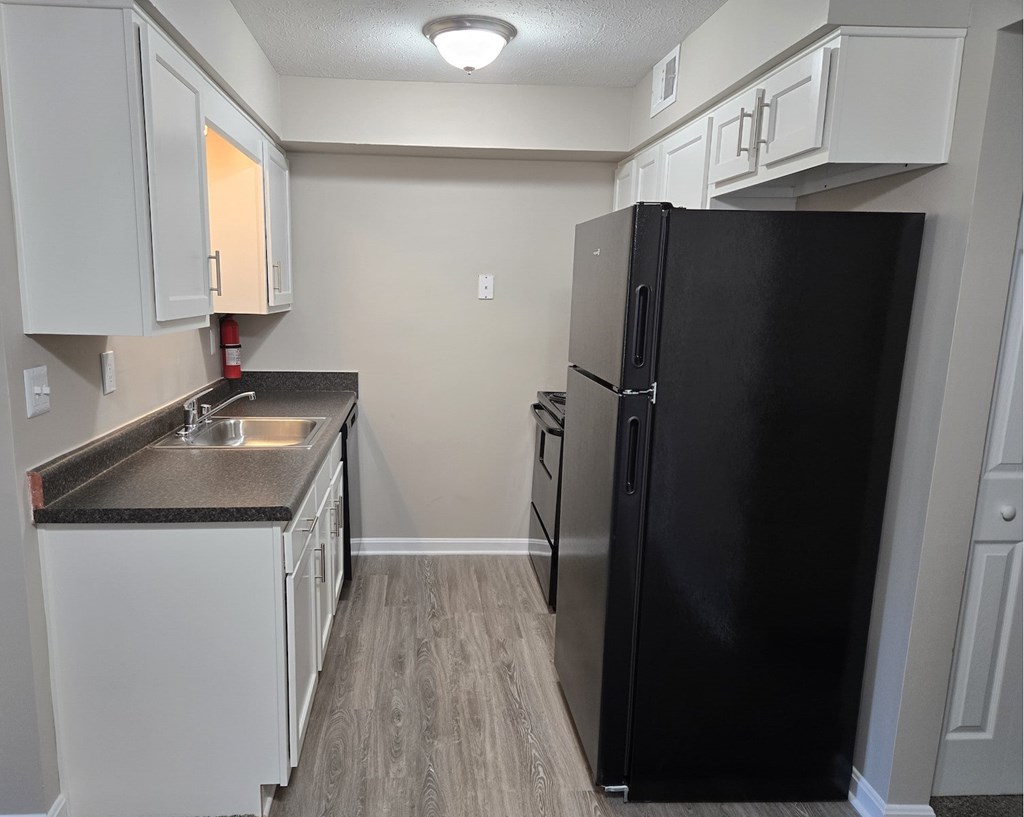 A black refrigerator sits in a kitchen with white cabinets.