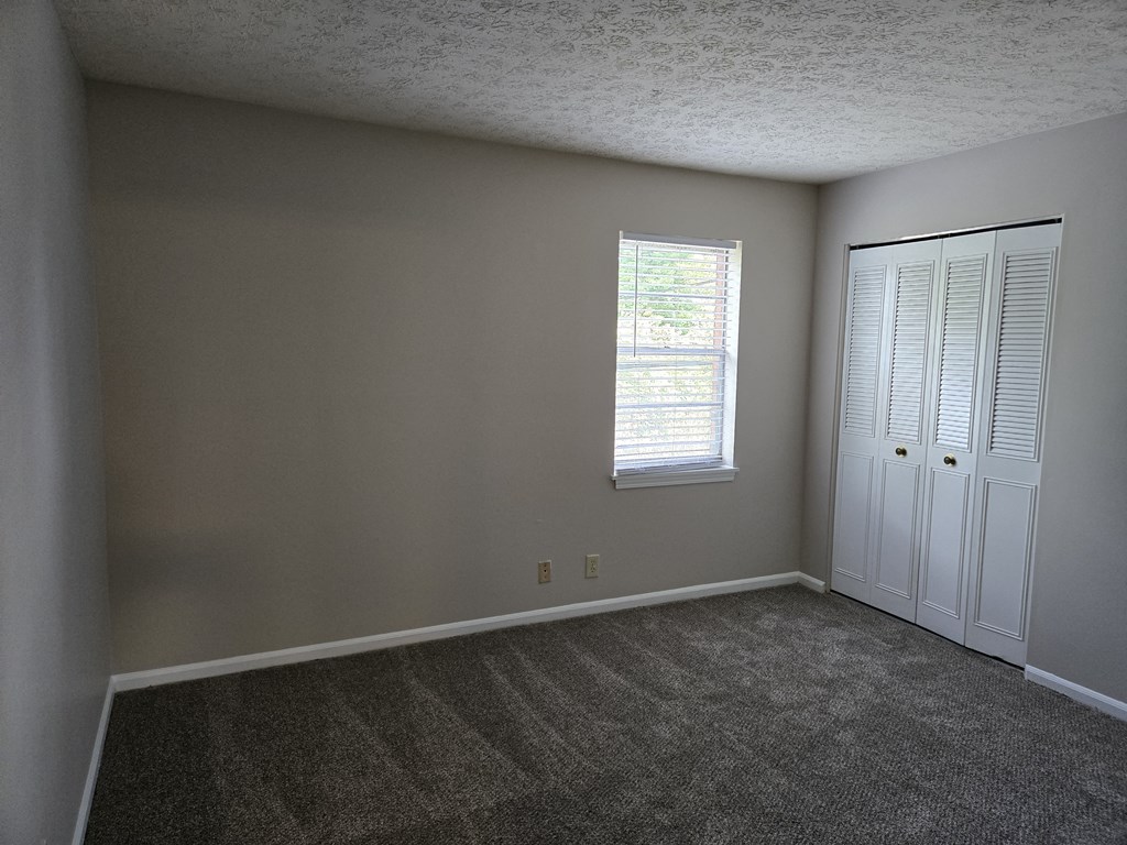 an empty room with carpet and a window and a closet