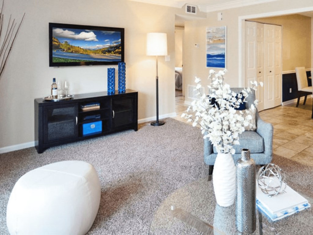 A living room with a grey sofa, a white ottoman, a black bookshelf, and a painting on the wall.