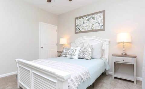 A white bedroom with a bed, nightstand, and a painting on the wall.