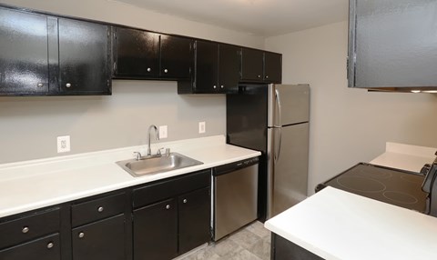 A kitchen with black cabinets and a stainless steel refrigerator.