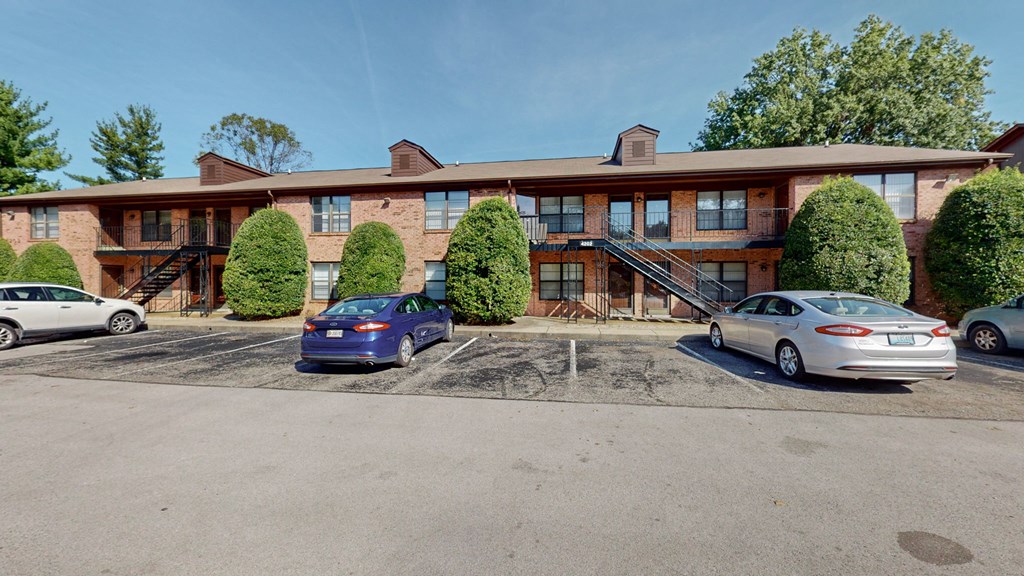 an empty parking lot in front of an apartment building with cars parked