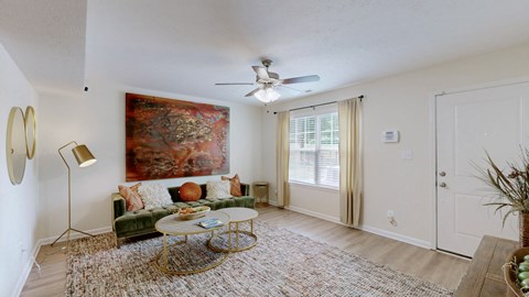 A living room with a green couch, a coffee table, a painting, and a ceiling fan.