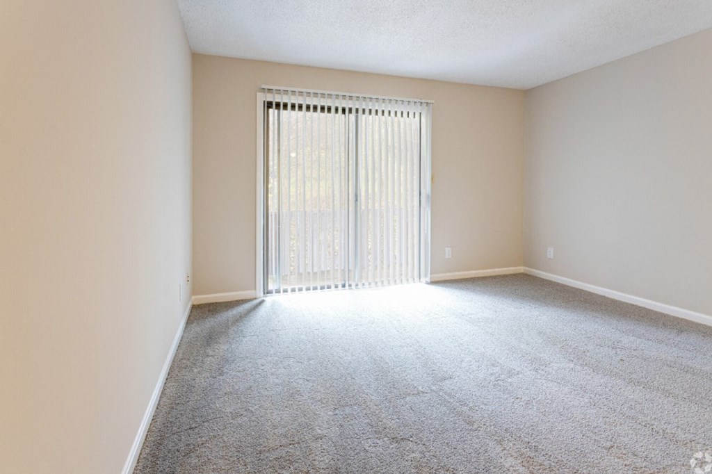 an empty living room with white carpet and a sliding glass door