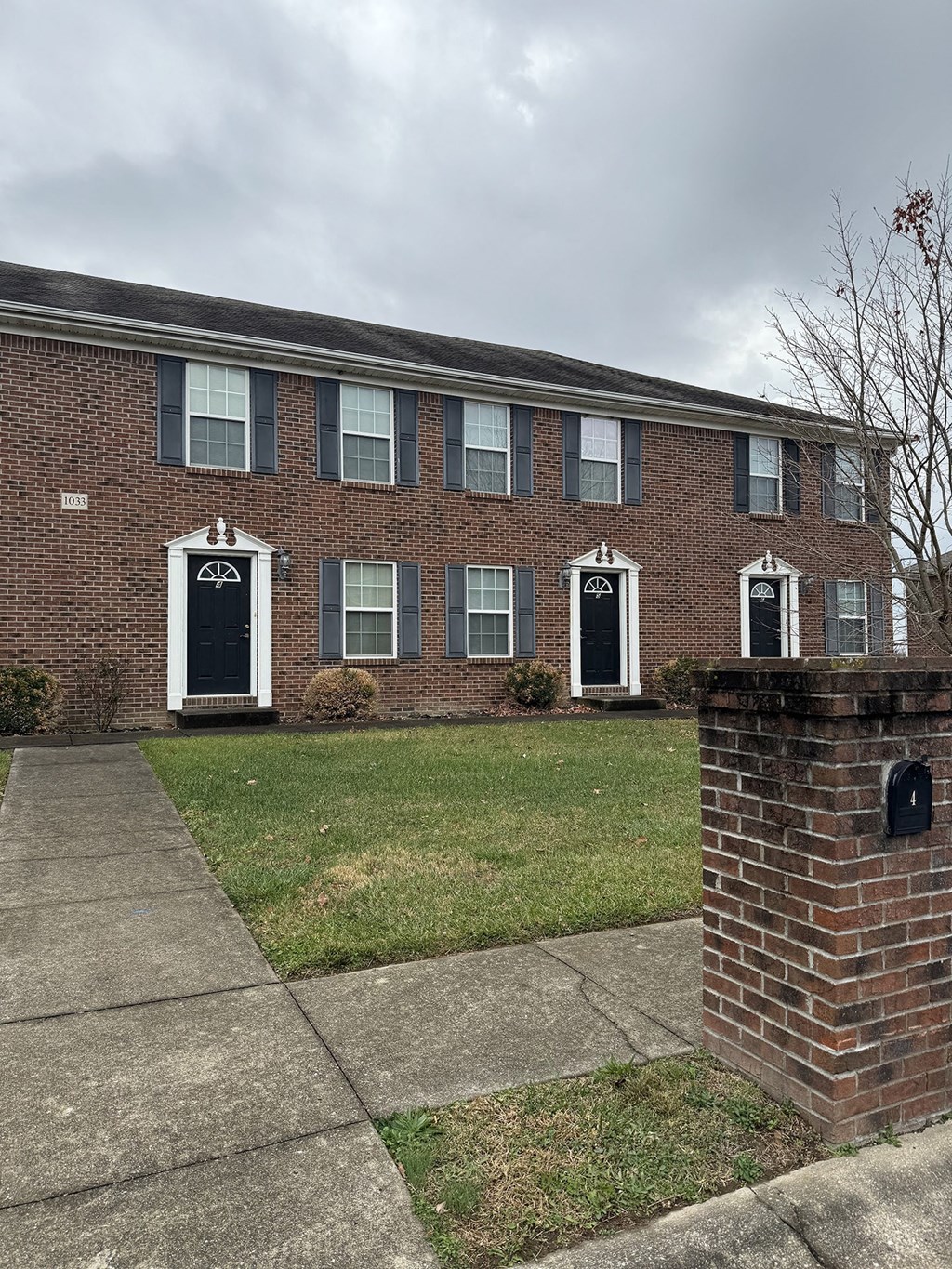 the front of a brick building with black doors and a sidewalk