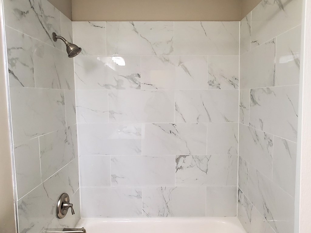 A white marble tiled shower with a silver shower head and faucet.