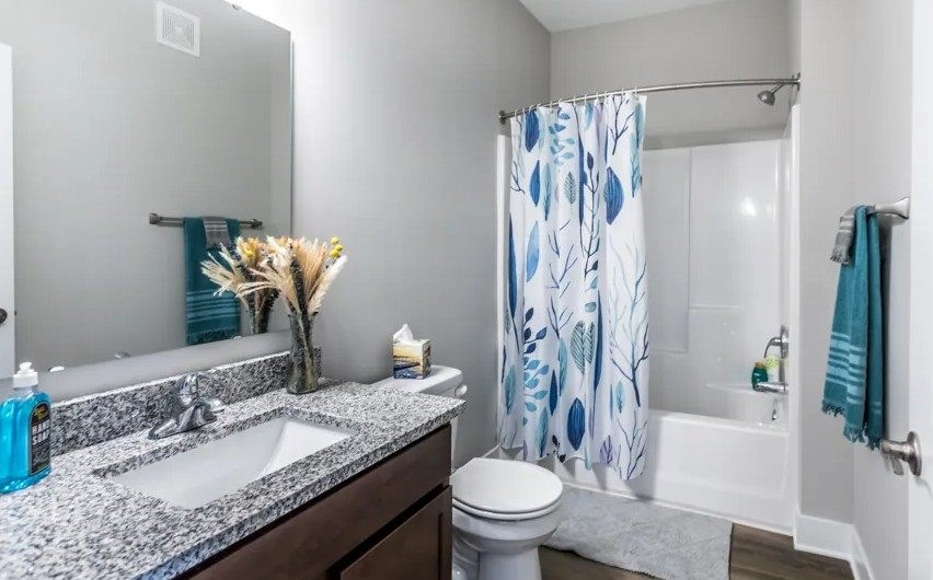 A bathroom with a white toilet, a sink, a shower curtain, and a mirror.