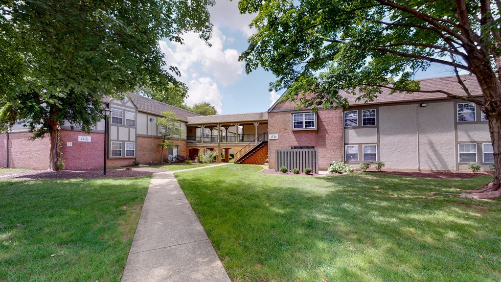 exterior view of a brick apartment building with a lawn and sidewalk