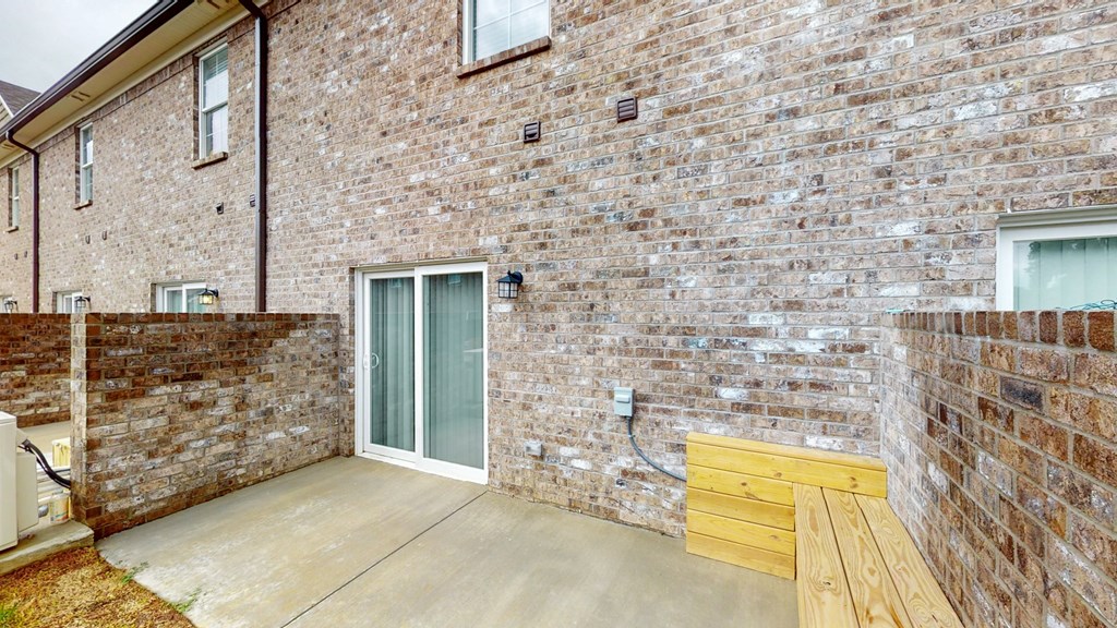 the patio of a brick house with a wooden bench