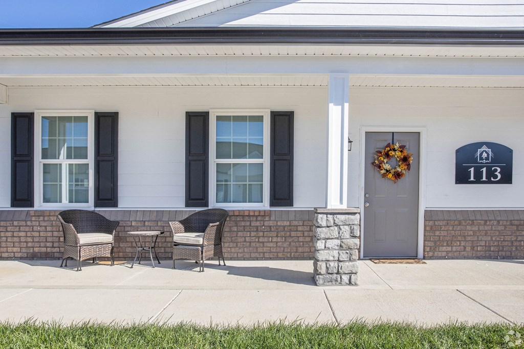 the front porch of a home with chairs and a wreath on the door