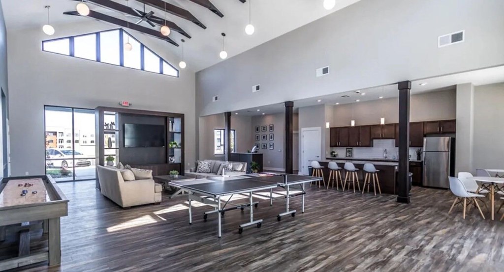 A spacious living room with a pool table and a kitchen area in the background.