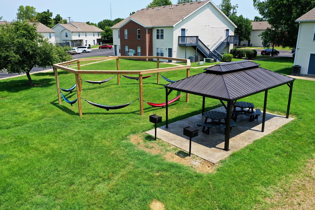 a picnic area with hammocks and a gazebo in a grassy yard