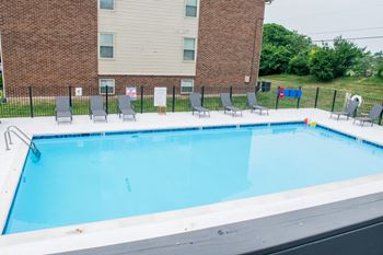 a swimming pool with chairs and a building in the background
