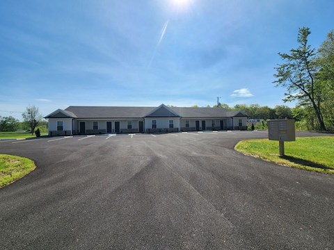 A large building with a grey roof and white walls is surrounded by a paved area.