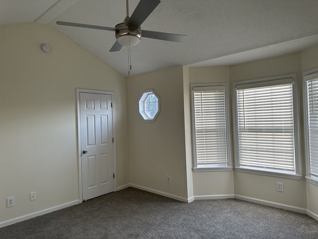 an empty bedroom with a ceiling fan and two windows