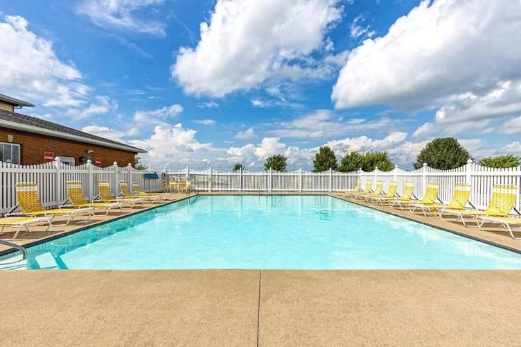 a swimming pool with yellow chairs and a white fence