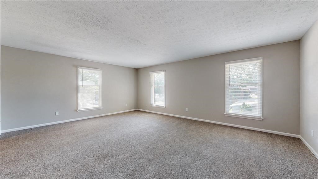 an empty living room with two windows and carpeting