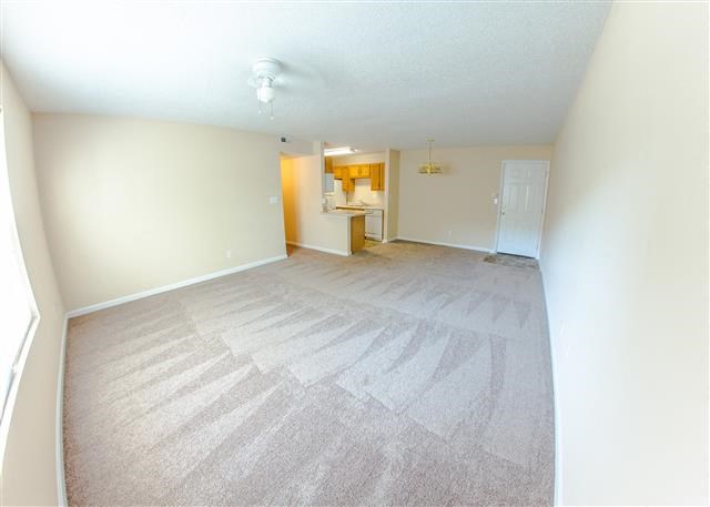 an empty living room with a kitchen in the background