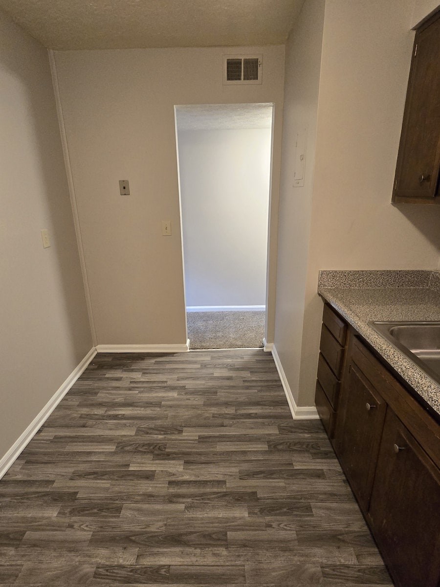 A hallway with a tiled floor and a sink in the corner.