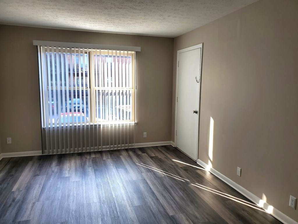 A room with a wooden floor and a window with blinds.