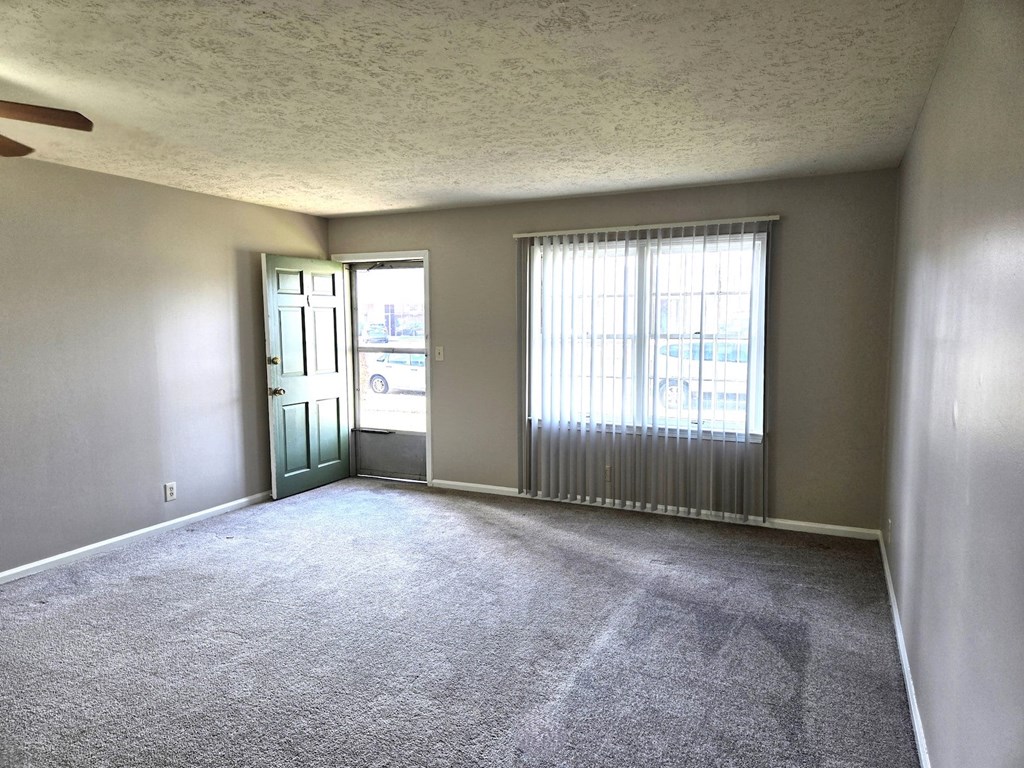 A room with a carpeted floor and a window with blinds.