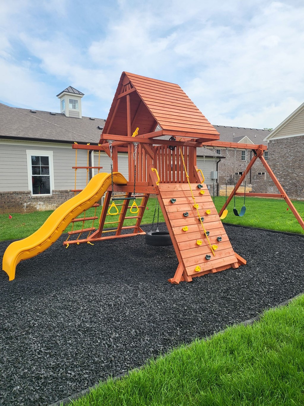 a wooden swing set with a yellow slide in a backyard