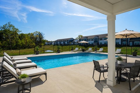 A pool surrounded by lounge chairs and a table under a white pergola.