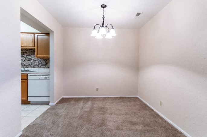 an empty living room with a kitchen in the background