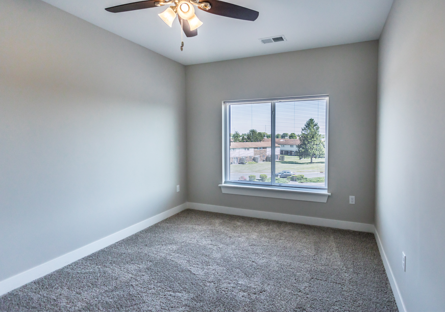 A room with a ceiling fan and a window overlooking a parking lot.