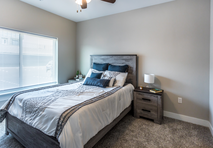 A bedroom with a large bed, a nightstand, and a window with blinds.