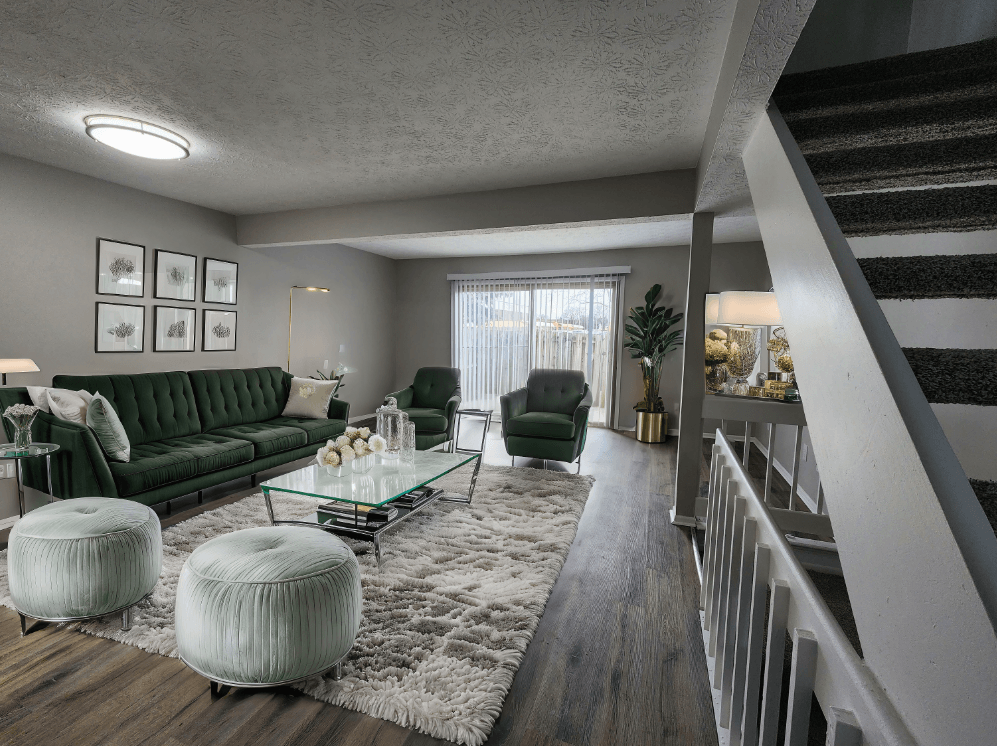 A living room with a green couch, a glass coffee table, and a staircase.