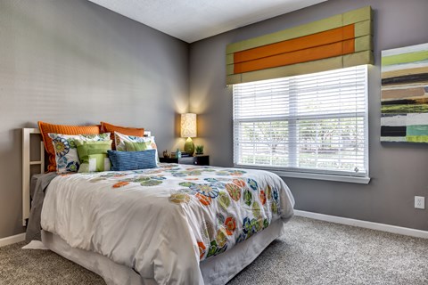 A bedroom with a large bed and a window with blinds.