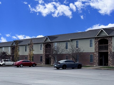 A red car is parked in front of a building with a stone pillar.