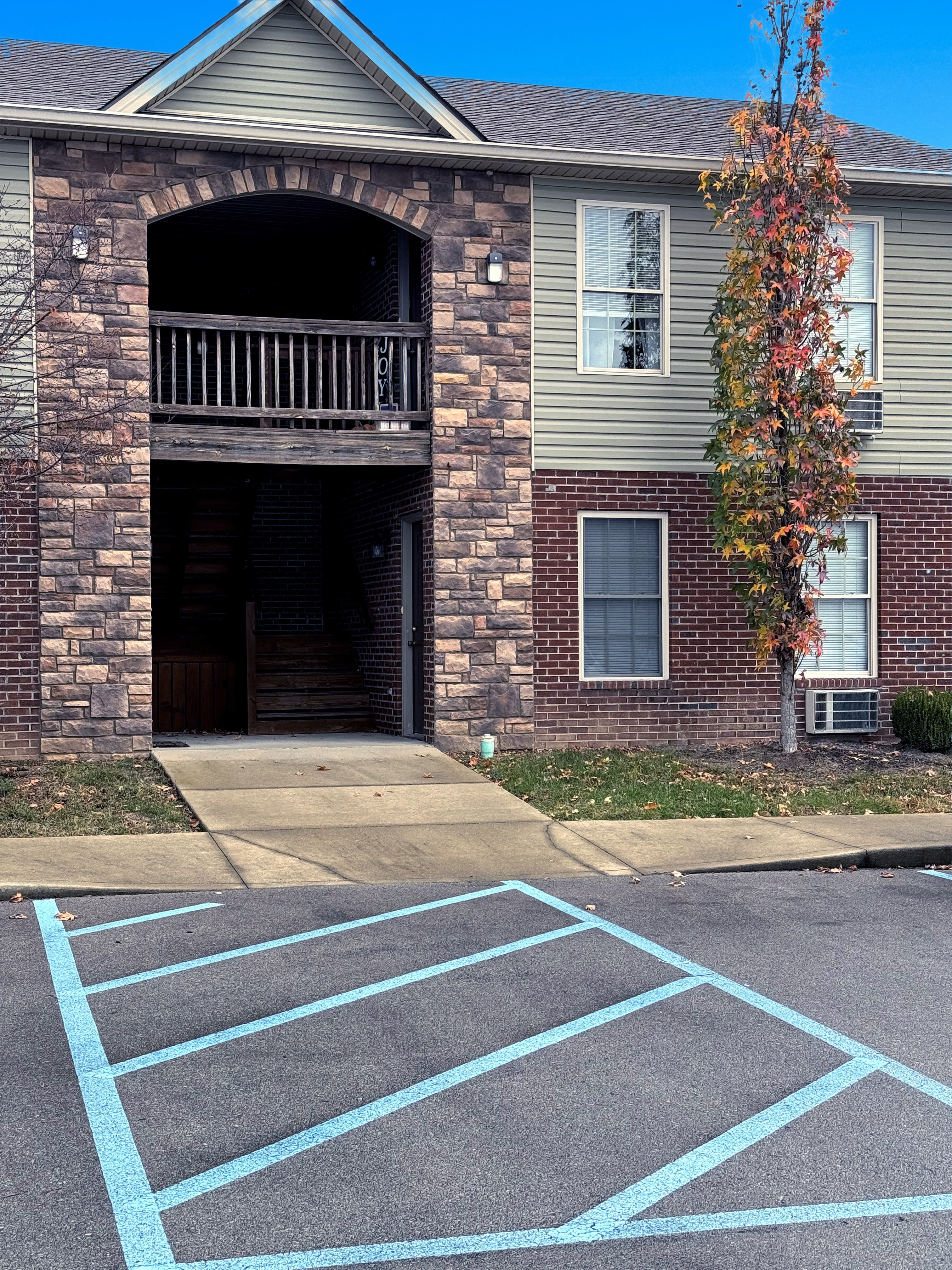 A tree with red leaves is in front of a grey house.