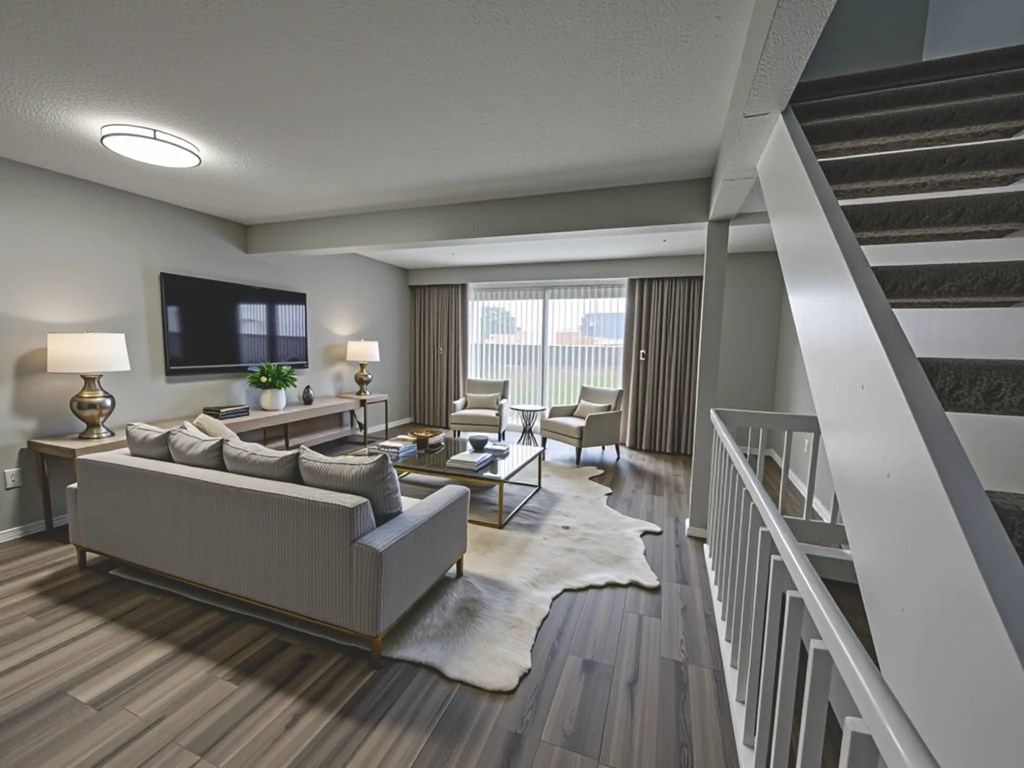 A living room with a grey couch, a white rug, and a staircase.