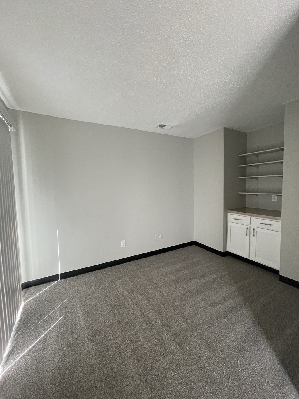 an empty living room with carpet and white cabinets and shelves