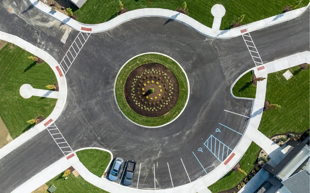 A roundabout with a flower bed in the center and cars parked on the side.