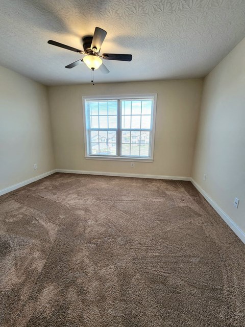an empty living room with a ceiling fan and a window