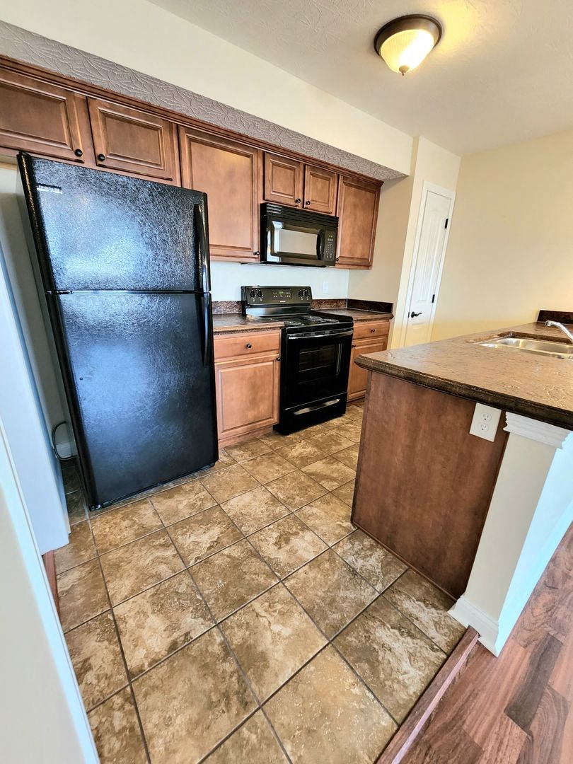 a kitchen with a black refrigerator and wooden cabinets