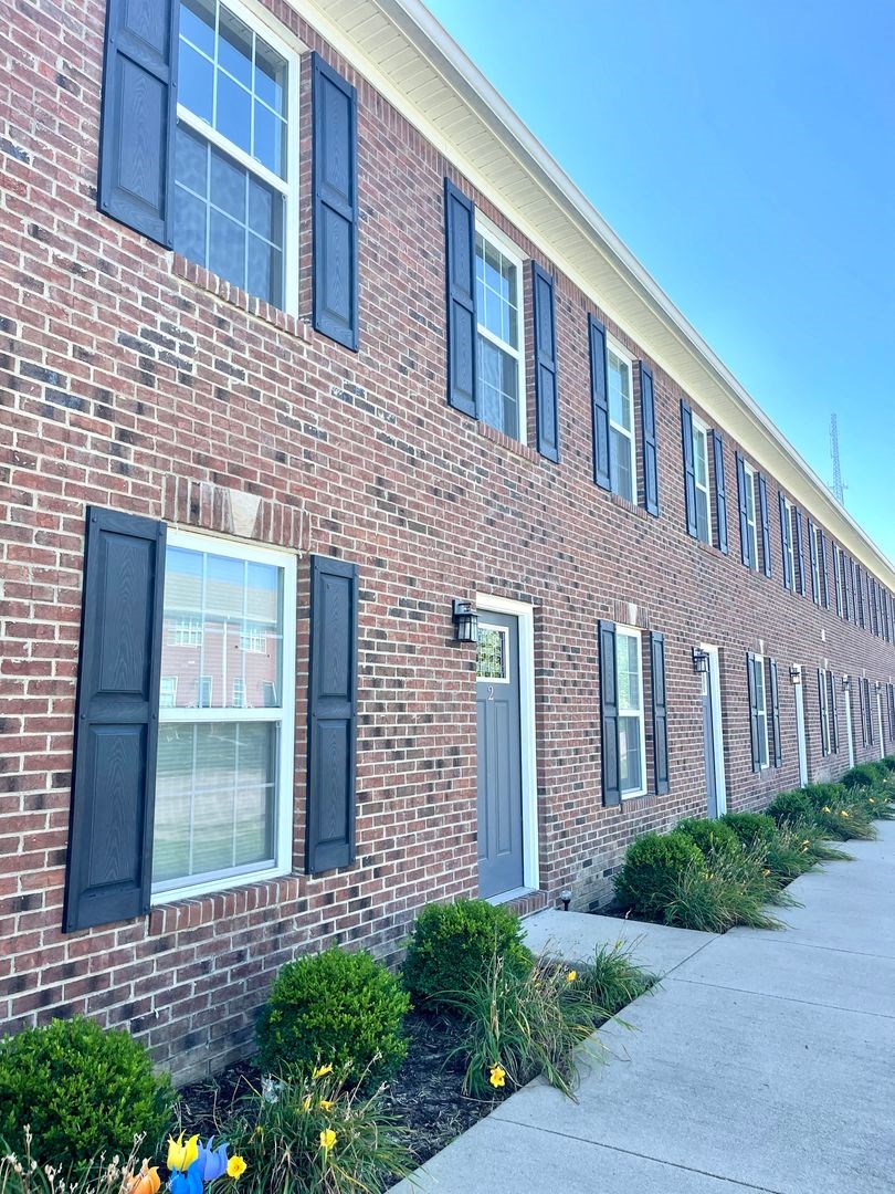 a brick building with black shuttered windows and a sidewalk