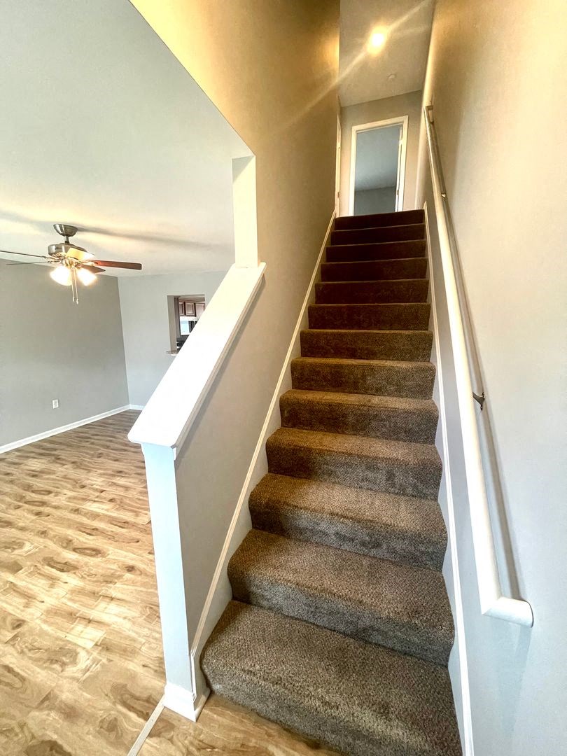 a carpeted staircase in a home with a ceiling fan