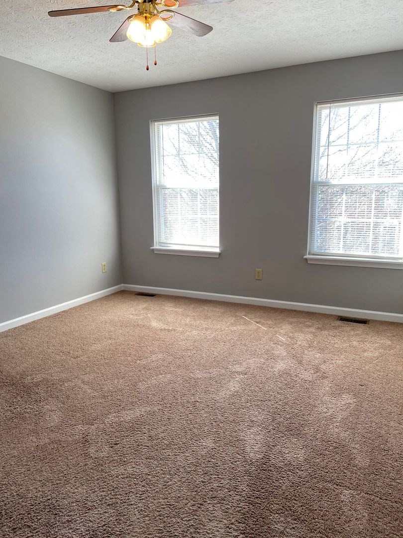 an empty room with a ceiling fan and two windows