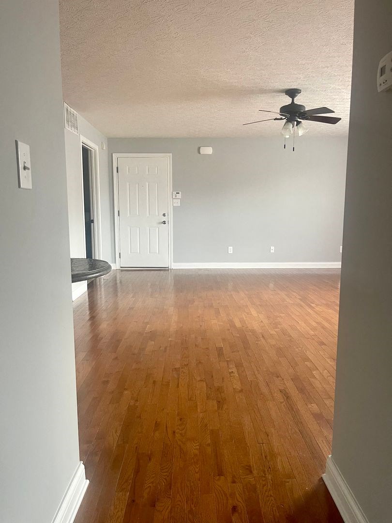 an empty living room with wood floors and a ceiling fan