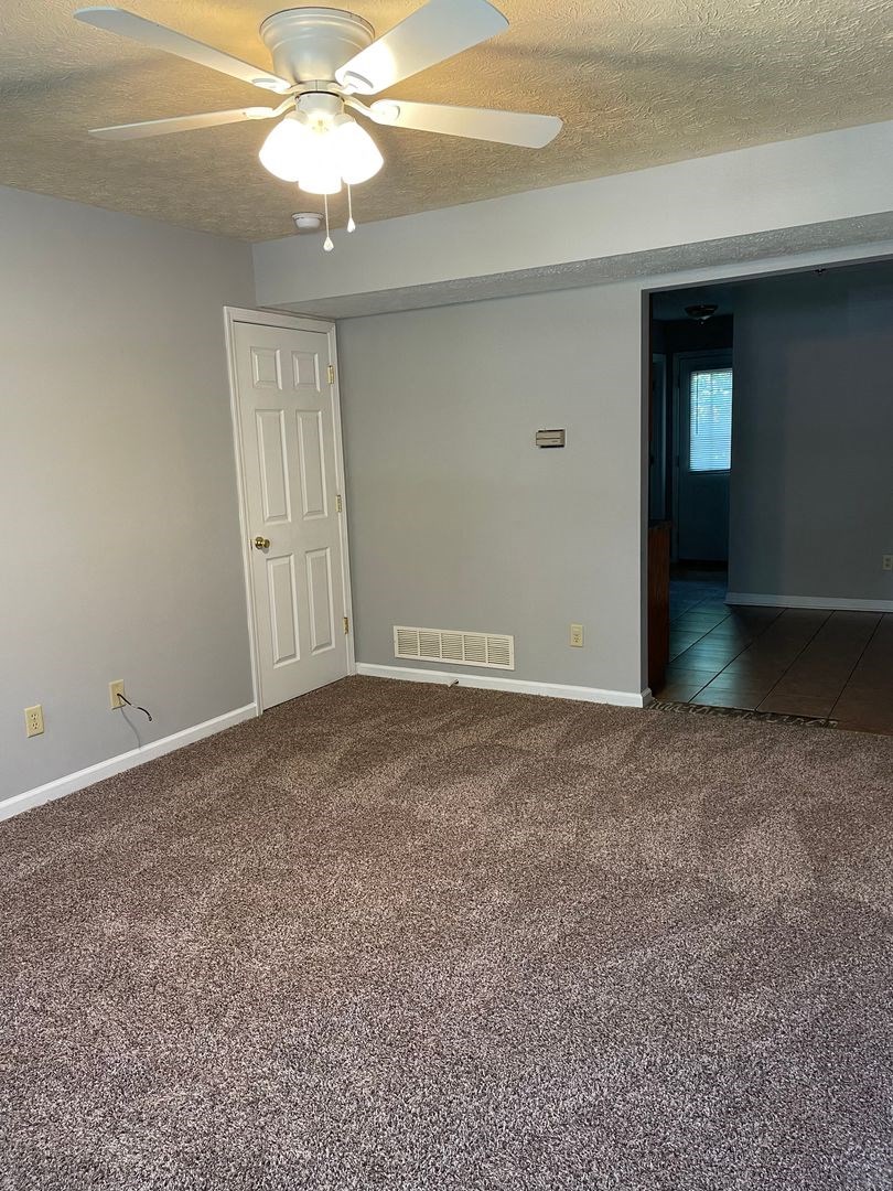 a empty living room with a ceiling fan and a carpet