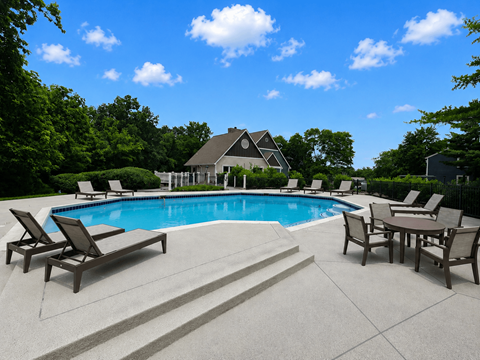A pool surrounded by chairs and a house in the background.