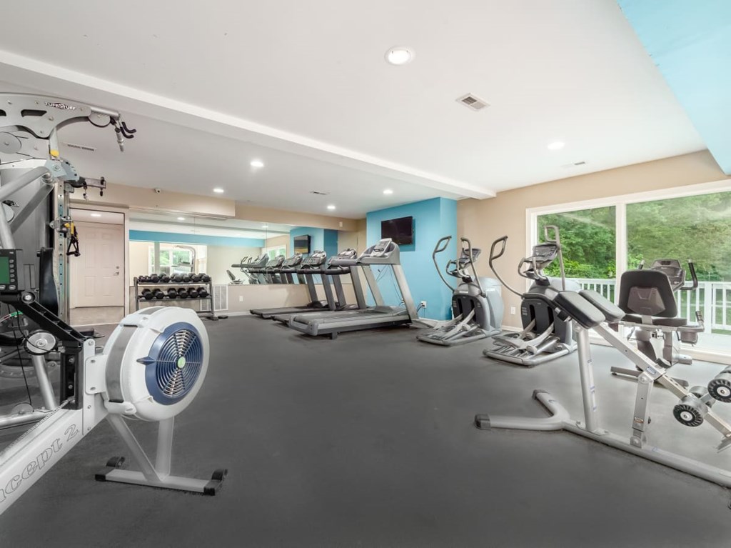 A spacious gym with a variety of exercise equipment including treadmills, elliptical machines, and a fan.