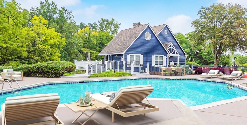 A poolside table with two chairs is in front of a blue house.