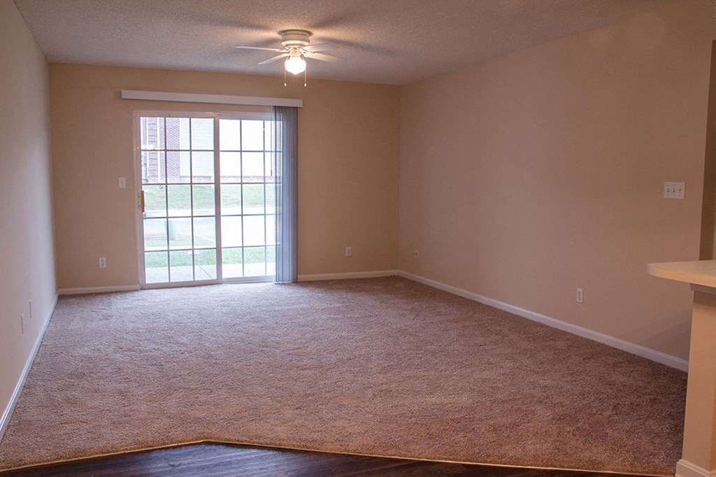 an empty living room with a window and a ceiling fan