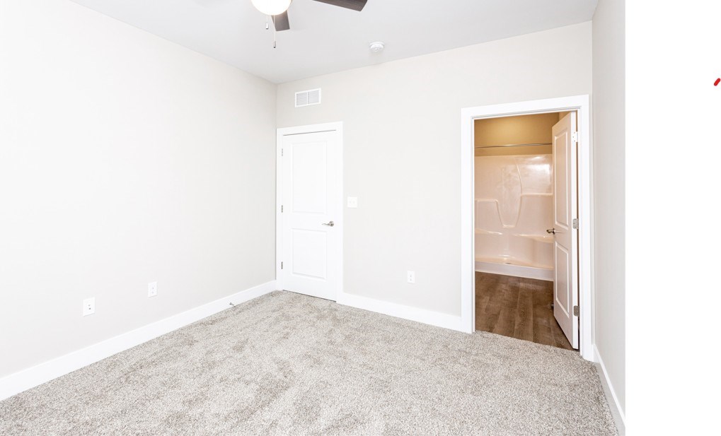 A room with a carpeted floor and a ceiling fan.