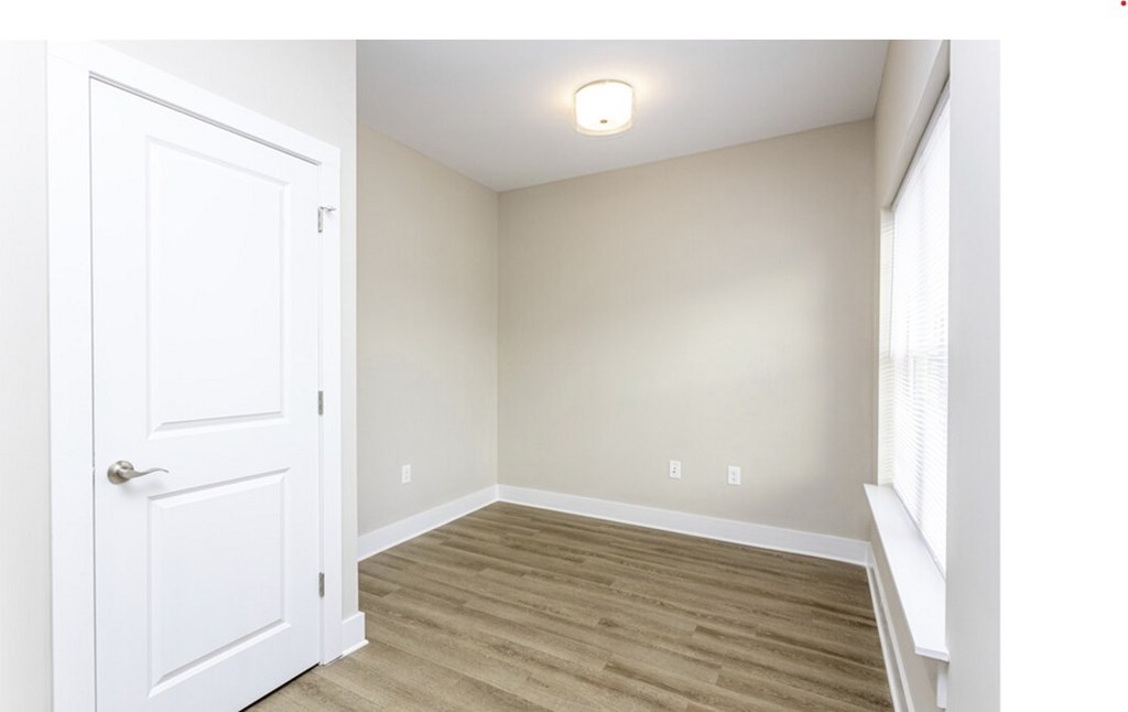 A white door is on the left side of a room with a light on the ceiling and a window on the right.